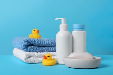 Photo of Baby cosmetic products, bath ducks and towels on light blue background