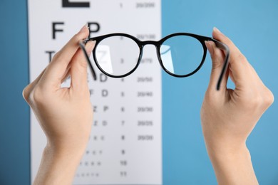 Photo of Woman holding glasses against eye chart on blue background, closeup. Ophthalmologist prescription