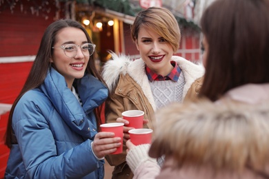 Happy friends with cups of mulled wine at winter fair