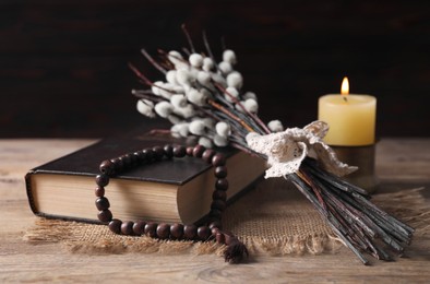 Photo of Rosary beads, Bible, burning candle and willow branches on wooden table, closeup