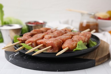 Photo of Wooden skewers with cut raw marinated meat on white tiled table, closeup