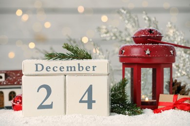 Photo of December 24 - Christmas Eve. Wooden block calendar and festive decor on snow against blurred lights
