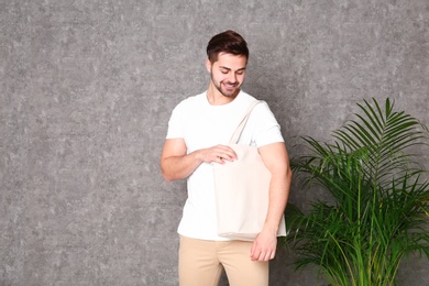 Portrait of young man with eco bag at indoor palm plant near grey wall