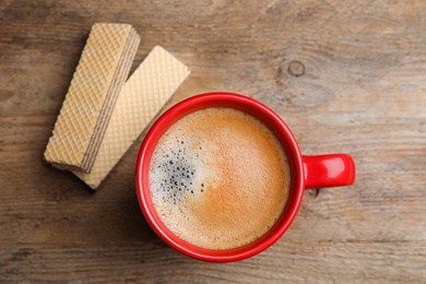 Delicious wafers and cup of coffee for breakfast on wooden table, flat lay