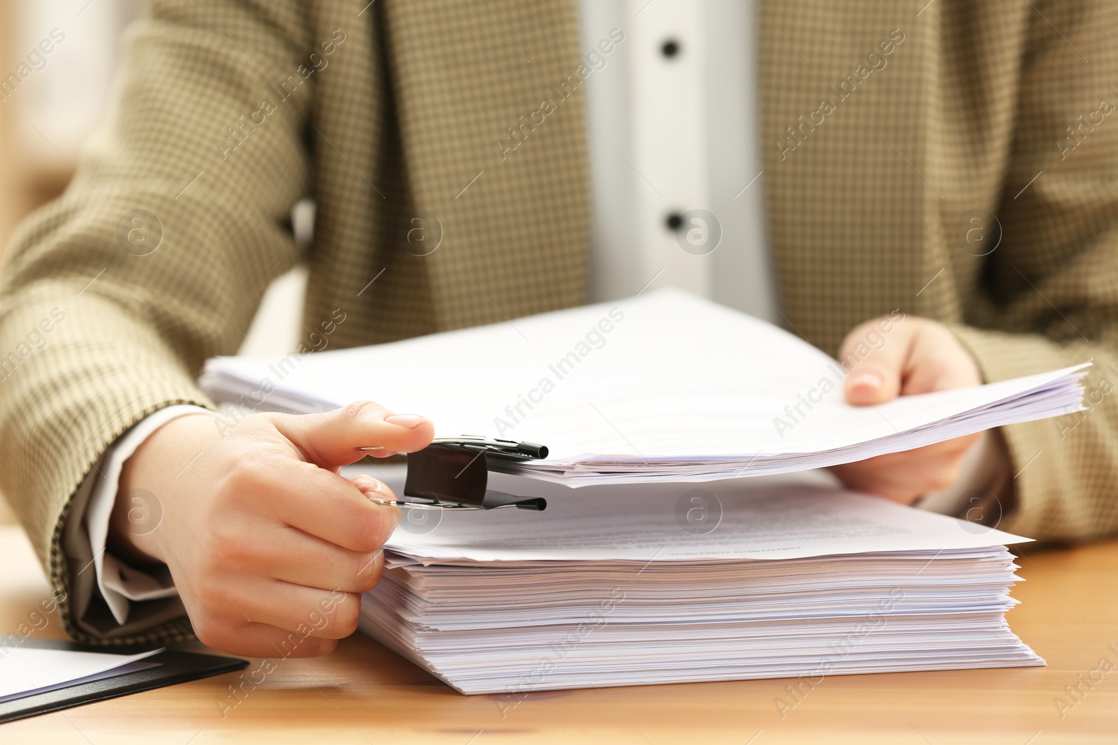 Photo of Woman attaching documents with metal binder clip at table in office, closeup