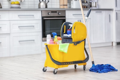 Photo of Mop bucket with cleaning supplies in kitchen