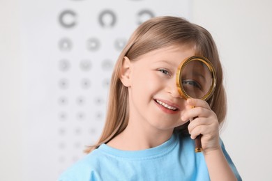 Little girl with magnifying glass against vision test chart