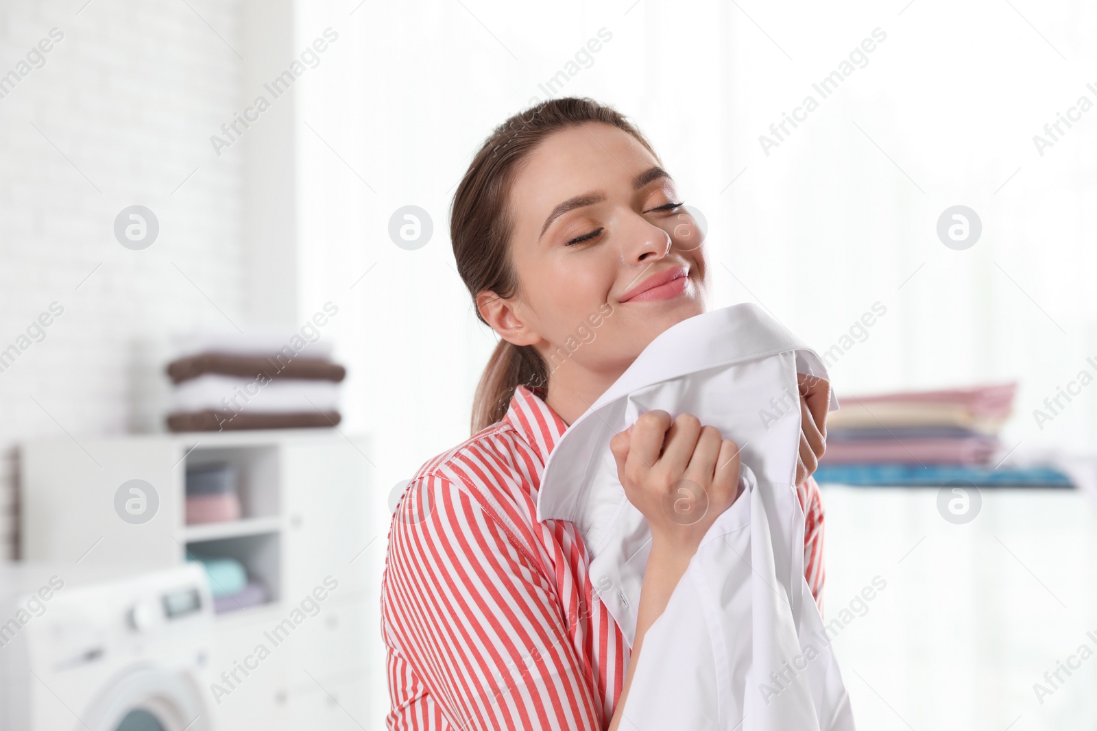 Photo of Happy young woman with clean shirt indoors. Laundry day