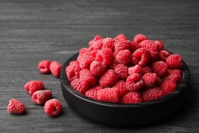 Photo of Bowl of delicious fresh ripe raspberries on dark wooden table, space for text