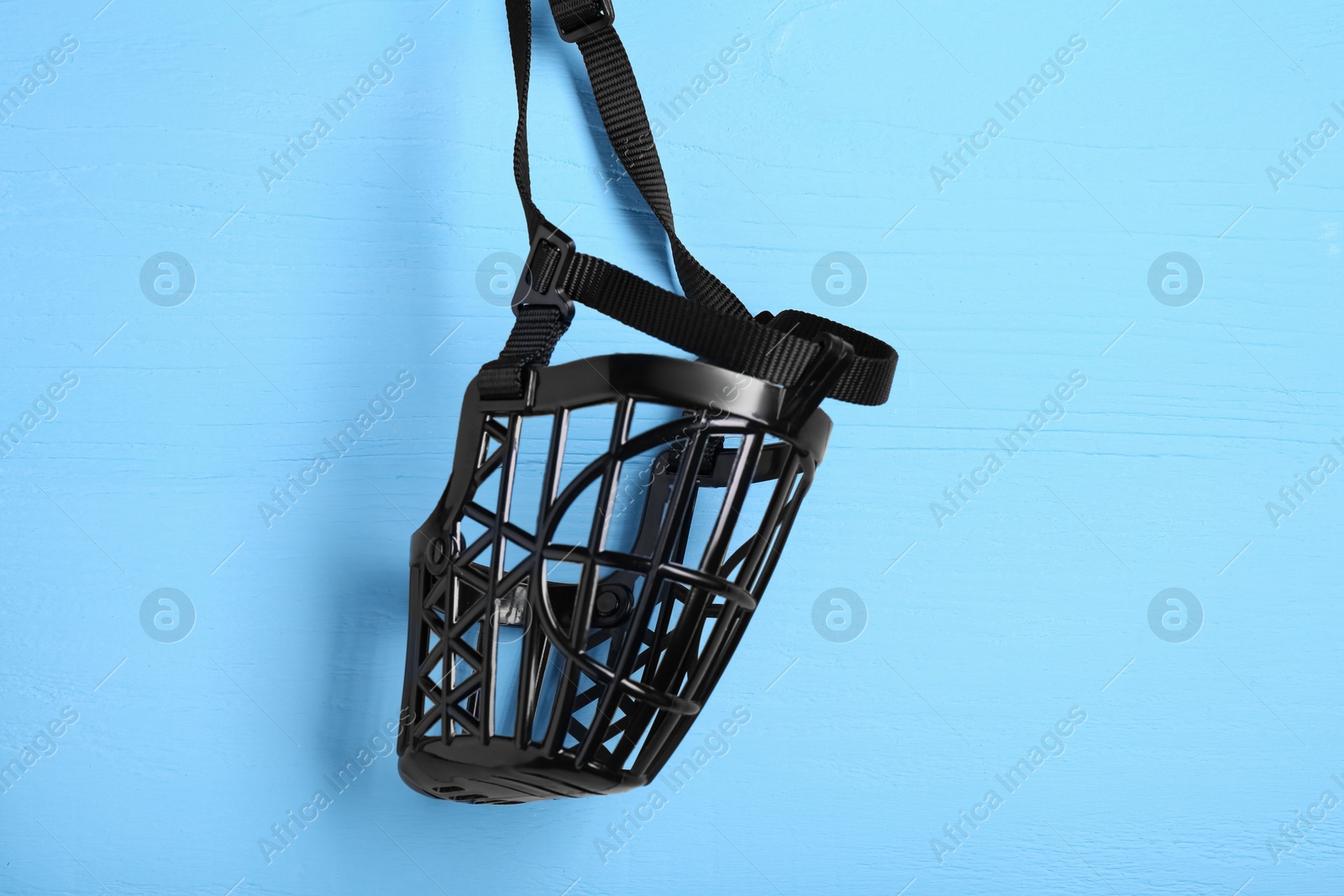 Photo of Black plastic dog muzzle on light blue wooden table, top view