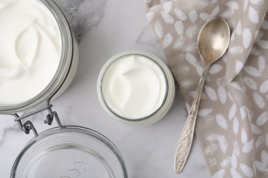 Delicious natural yogurt in glass jars and spoon on white marble table, top view