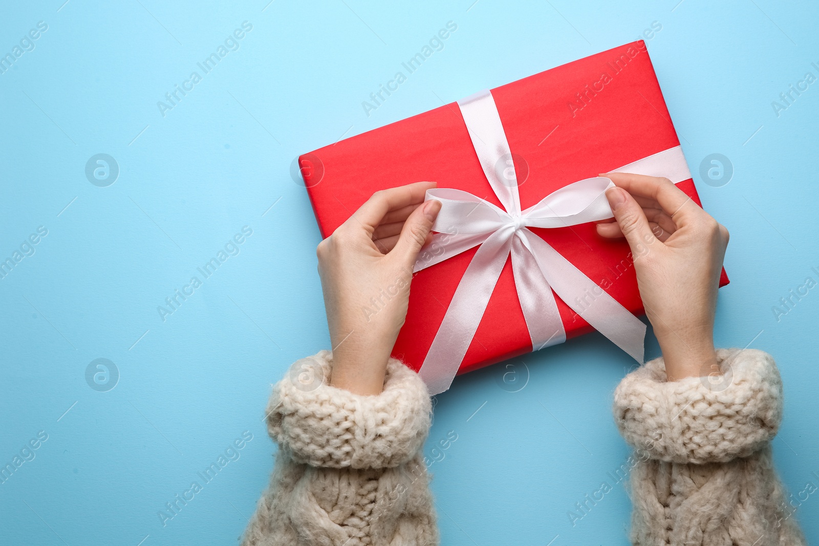 Photo of Woman holding red Christmas gift box on light blue background, top view