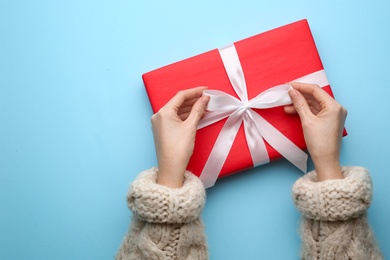 Photo of Woman holding red Christmas gift box on light blue background, top view