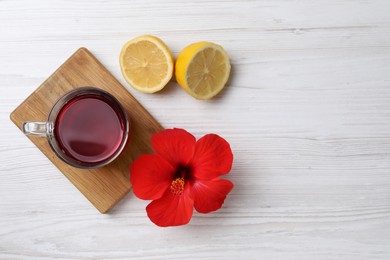 Delicious hibiscus tea, halves of lemon and beautiful flower on white wooden table, flat lay. Space for text