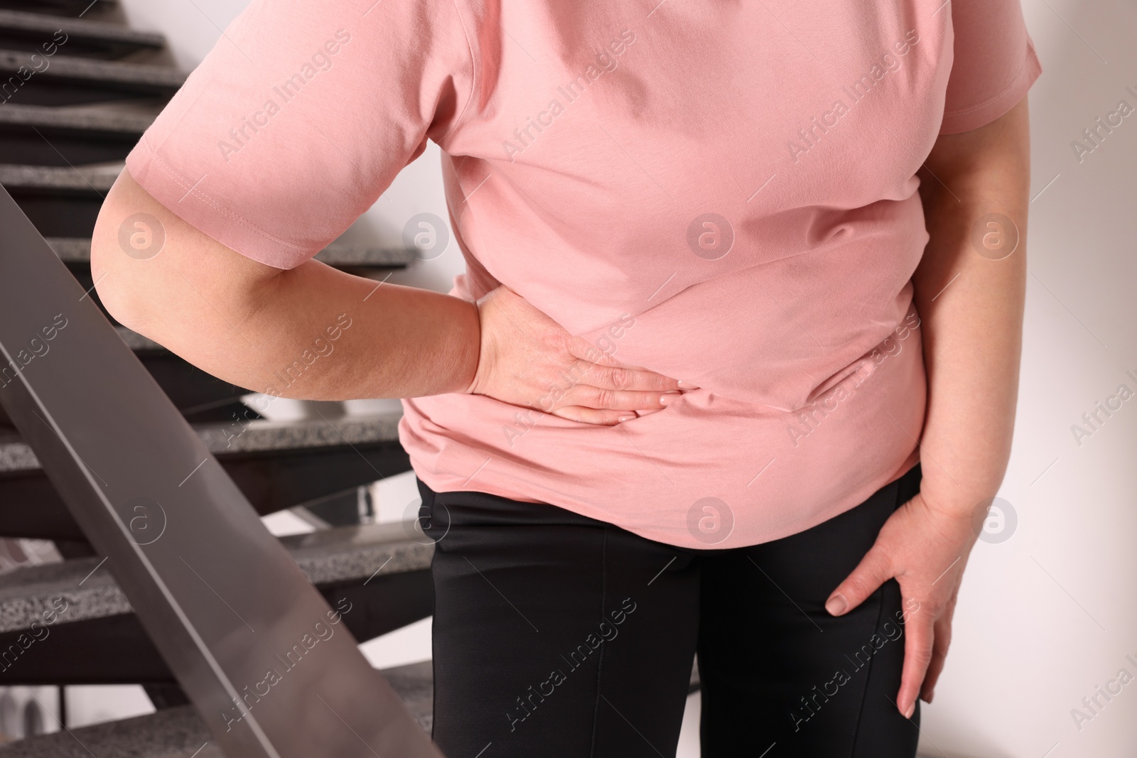 Photo of Overweight mature woman suffering from pain in right side on stairs indoors, closeup