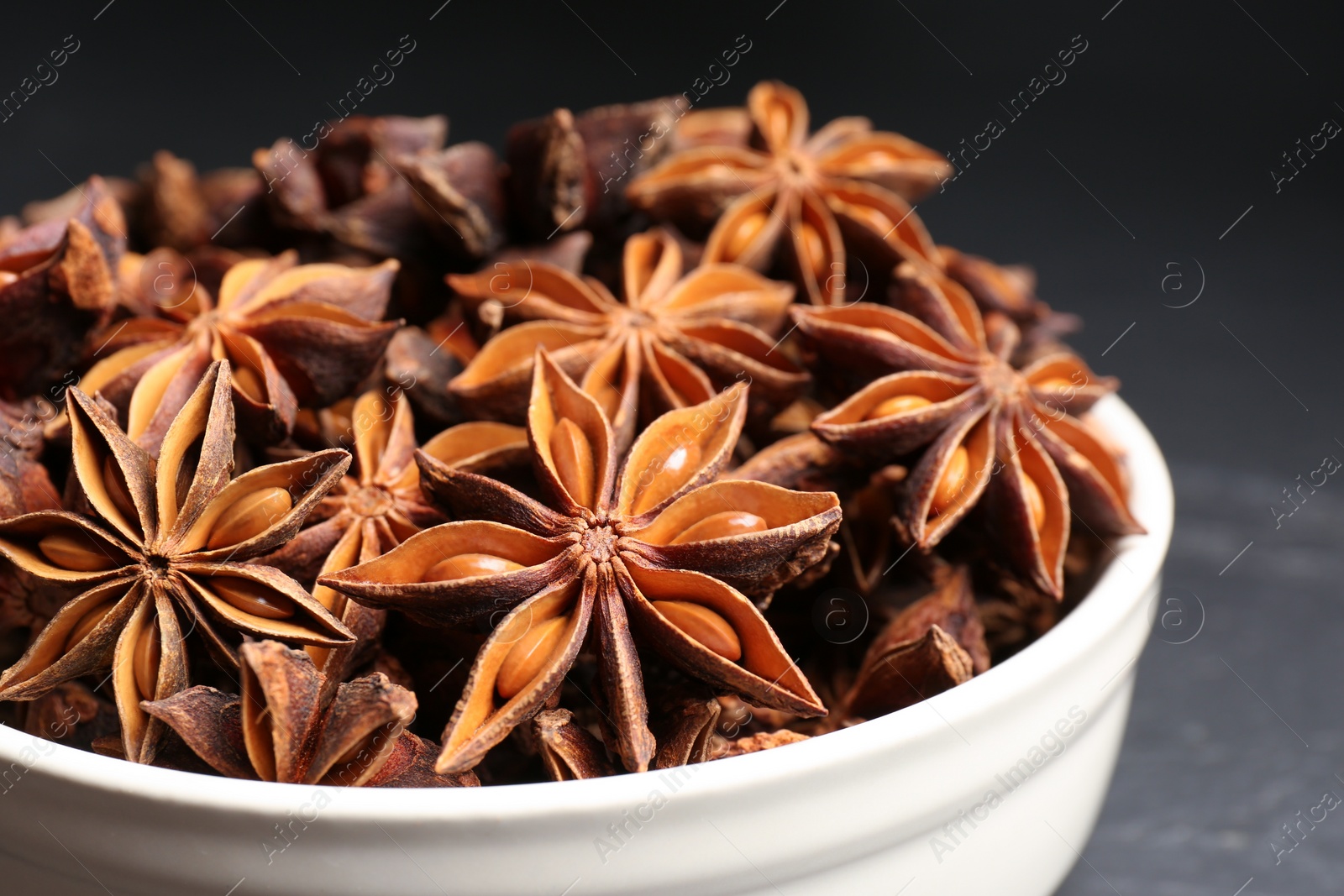 Photo of Bowl with aromatic anise stars on dark table, closeup