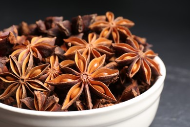 Photo of Bowl with aromatic anise stars on dark table, closeup