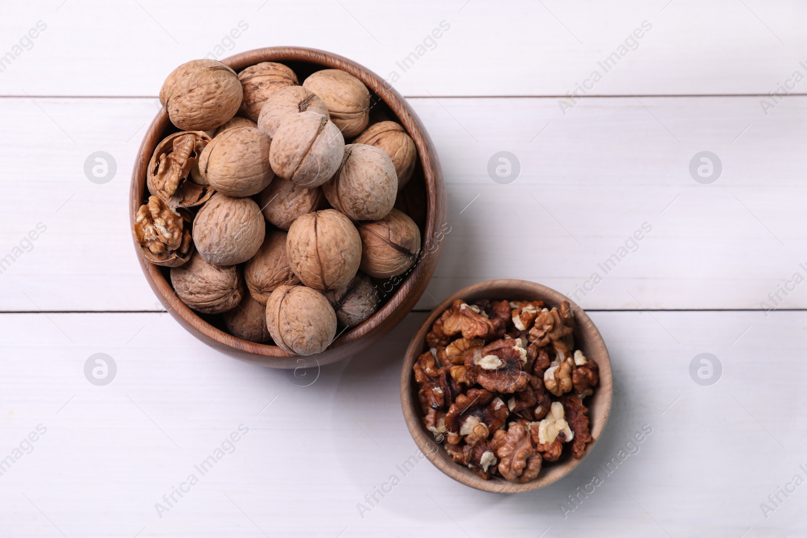 Photo of Bowls with walnuts on white wooden table, flat lay
