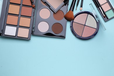 Colorful contouring palettes and brushes on light blue background, flat lay with space for text. Professional cosmetic product