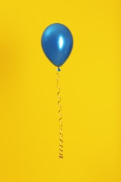 Bright balloon with ribbon on color background