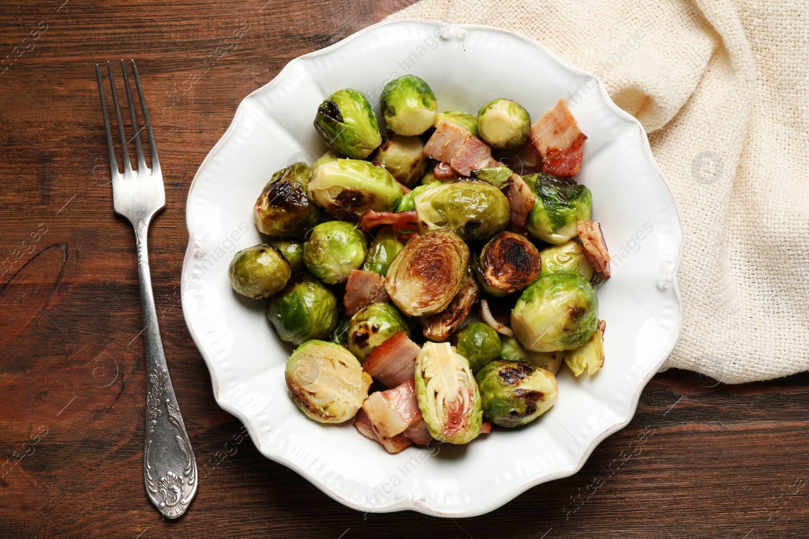 Photo of Delicious Brussels sprouts with bacon served on wooden table, flat lay