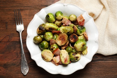 Delicious Brussels sprouts with bacon served on wooden table, flat lay