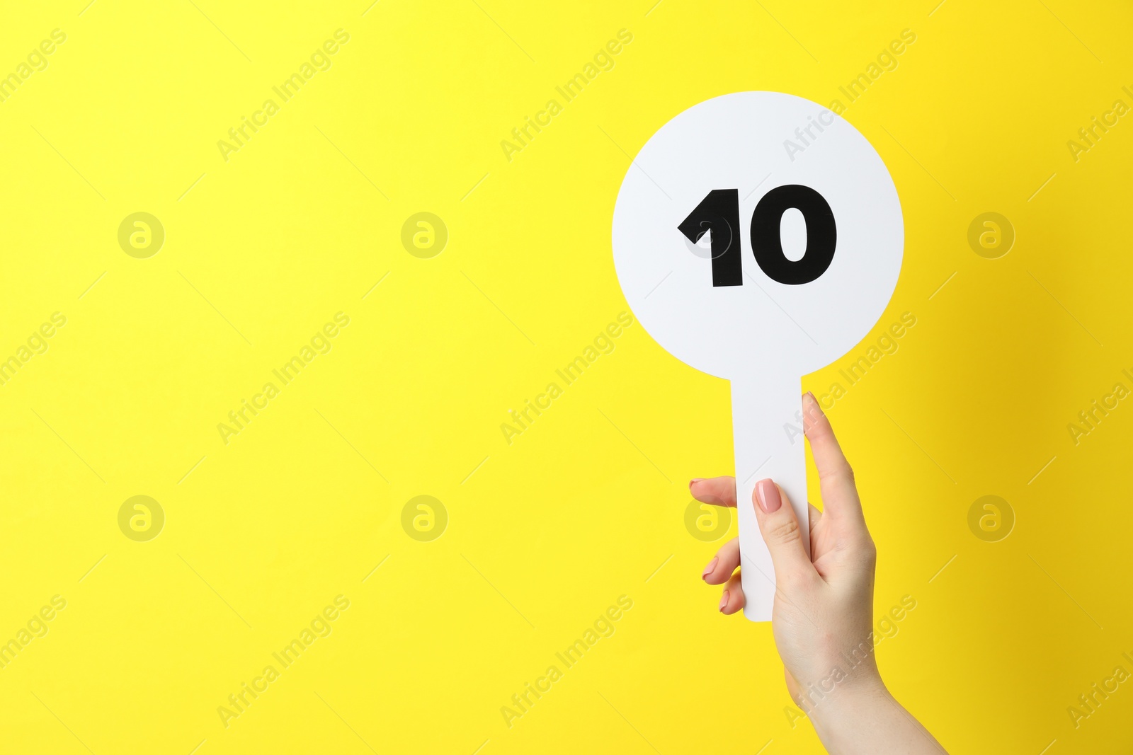 Photo of Woman holding auction paddle with number 10 on yellow background, closeup. Space for text