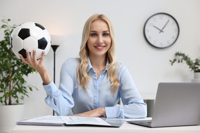 Photo of Happy woman with soccer ball at table in office