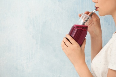 Woman holding bottle of beet smoothie on light background with space for text, closeup