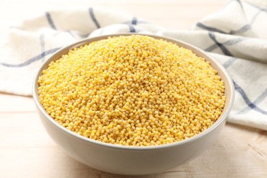 Photo of Millet groats in bowl on light wooden table, closeup