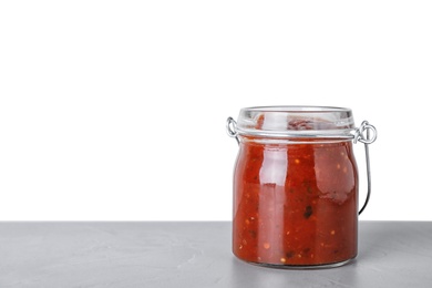 Photo of Glass jar of hot chili sauce on table against white background. Space for text