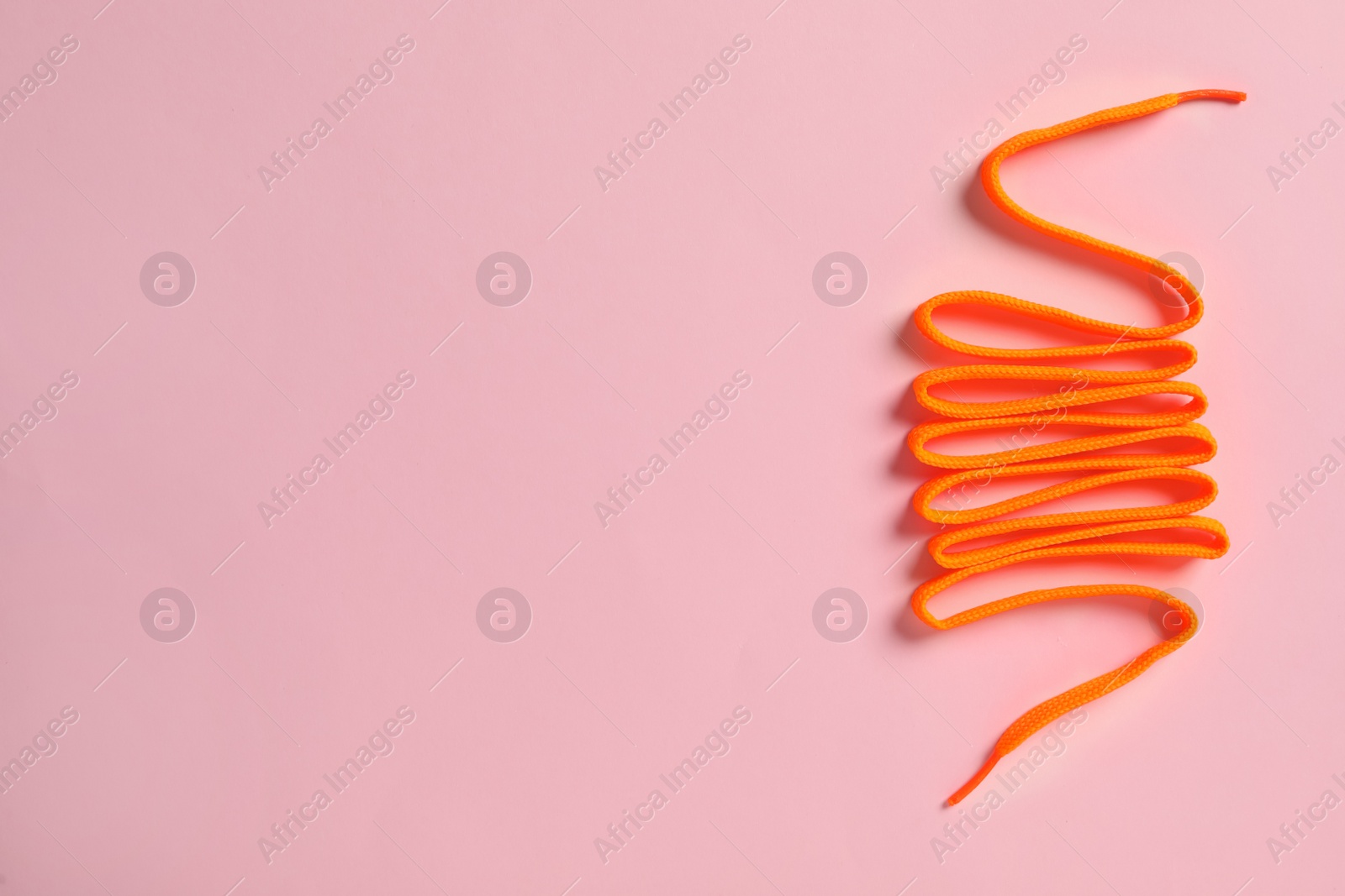 Photo of Orange shoelace on pink background, top view. Space for text