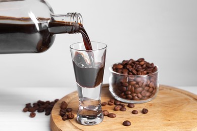 Photo of Pouring coffee liqueur from bottle into glass and beans at light table