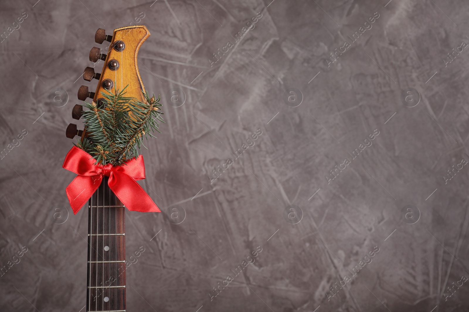 Photo of Guitar with fir tree branch and red bow on grey background, space for text. Christmas music