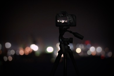 Image of Taking photo of with camera mounted on tripod. Blurred view of city lights at night, bokeh effect