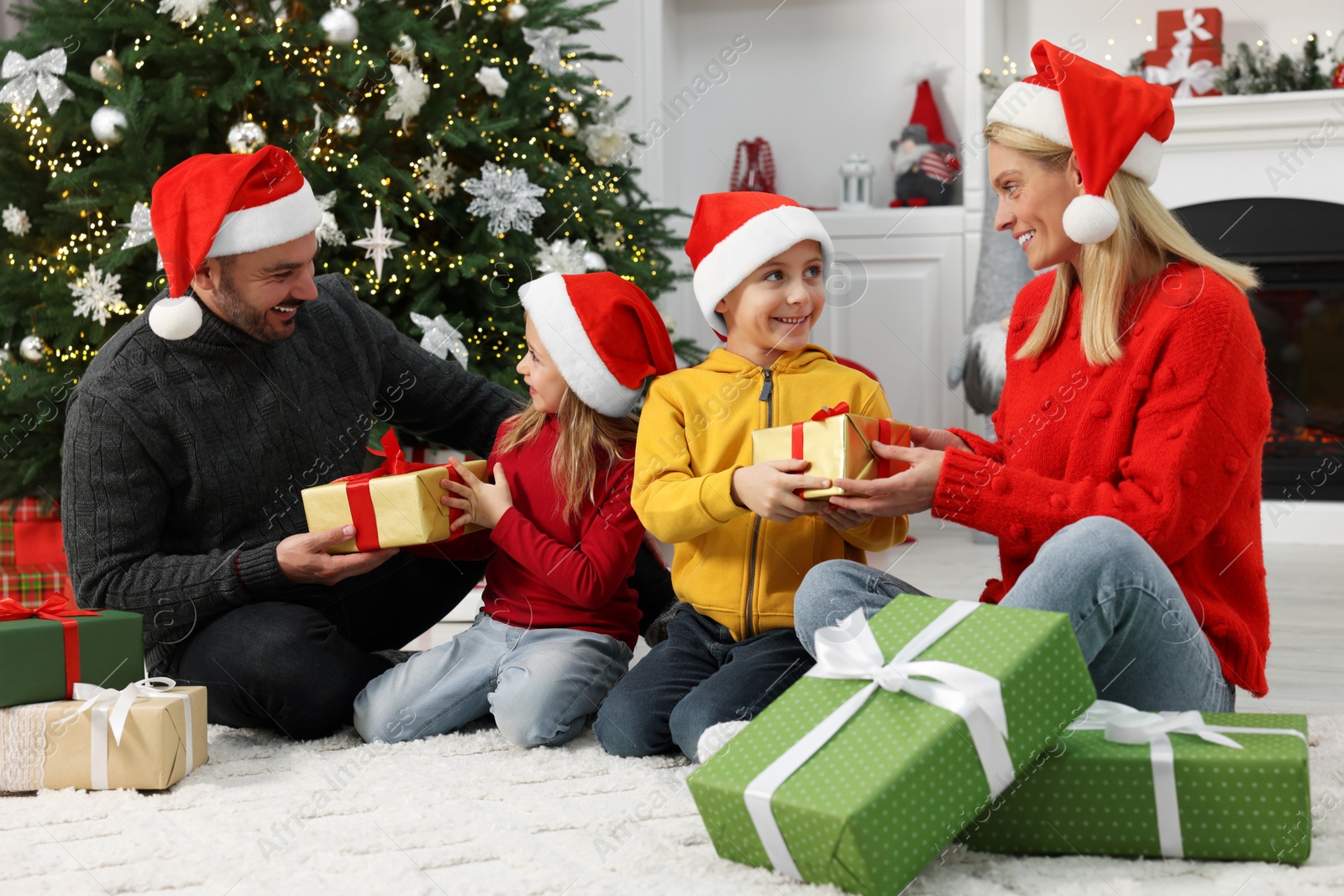 Photo of Happy family in Santa hats with Christmas gifts at home