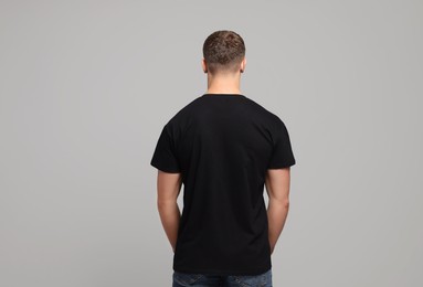 Man wearing black t-shirt on light grey background, back view. Mockup for design