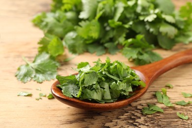 Photo of Fresh green cilantro and spoon on wooden table, closeup