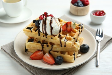 Photo of Delicious Belgian waffles with ice cream, berries and chocolate sauce served on white wooden table, closeup
