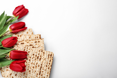 Photo of Tasty matzos and flowers on white background, flat lay with space for text. Passover (Pesach) Seder