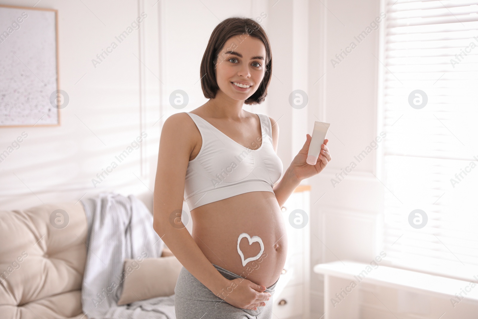 Photo of Young pregnant woman with cosmetic product at home