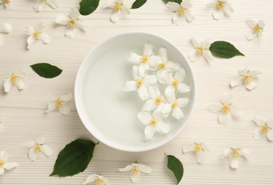 Bowl with water and beautiful jasmine flowers on white wooden table, flat lay