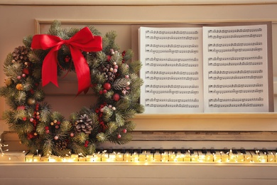 Photo of White piano with decorative wreath and note sheets. Christmas music