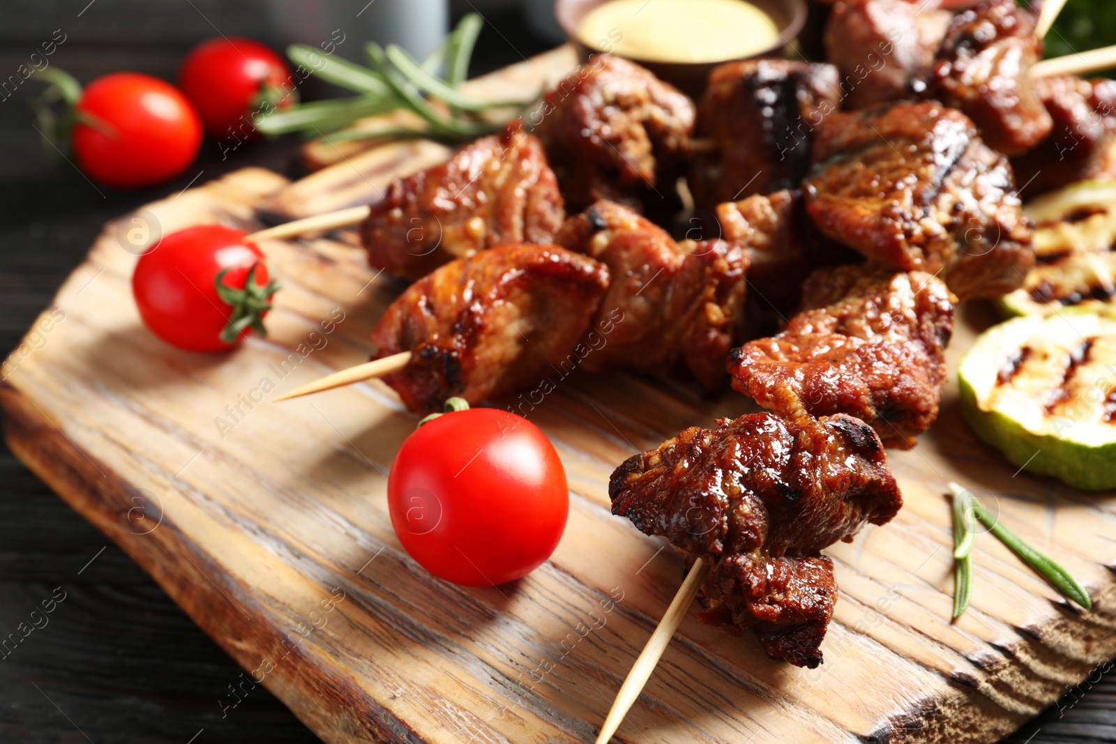 Photo of Delicious barbecued meat served with garnish and sauce on wooden board, closeup