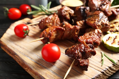 Photo of Delicious barbecued meat served with garnish and sauce on wooden board, closeup