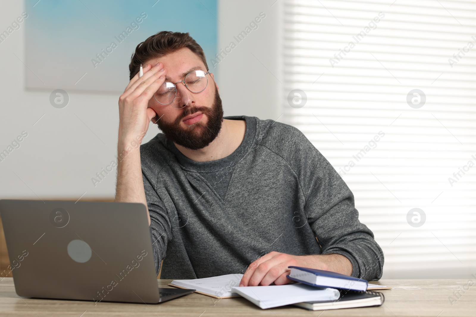 Photo of Overwhelmed man sitting with laptop at table indoors