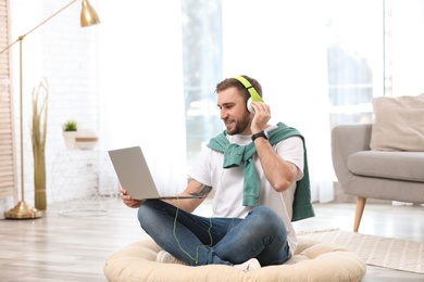Photo of Young man with headphones and laptop sitting on floor in living room