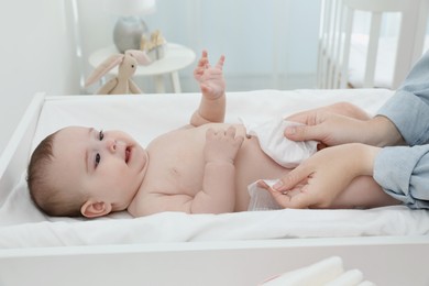 Mother changing baby's diaper on table at home