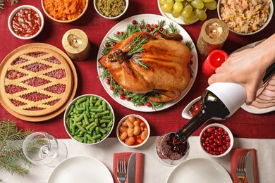 Photo of Woman pouring wine into glass at table with delicious roasted turkey for festive dinner, top view