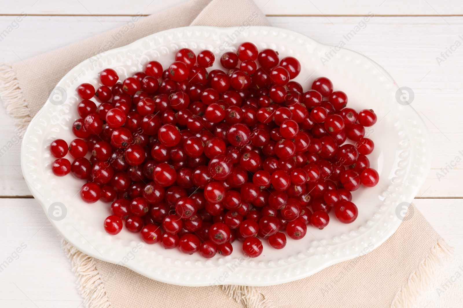 Photo of Plate with ripe red currants on white wooden table, above view